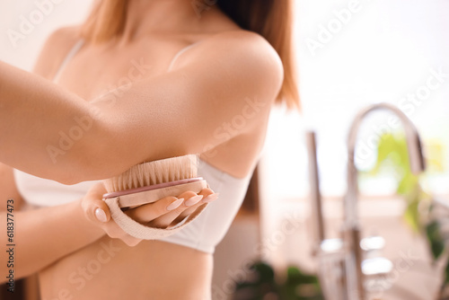 Young woman massaging her arm with anti-cellulite brush in bathroom, closeup