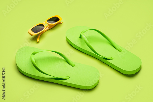 Green flip-flops with sunglasses on color background