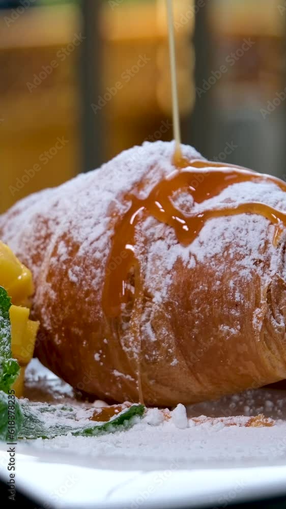 watering croissant with liquid caramel on white plate mango mint leaves