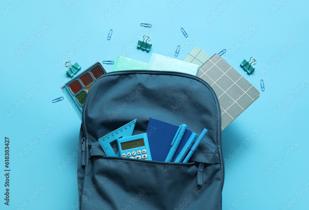 Naklejka premium School backpack with notebooks, calculator and watercolors on blue background