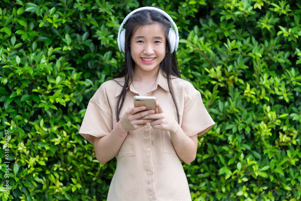 young asian girl using smartphone holding mobile phone device with wearing white wireless headphones and listening to music and using in the park outdoors or at the cafe in the sunny weather day young asian girl using smartphone holding mobile phone device with wearing white wireless headphones and listening to music and using in the park outdoors or at the cafe in the sunny weather day