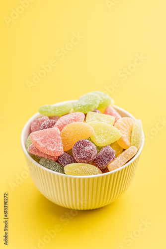 Mix of fruity jelly candy in bowl on yellow background.