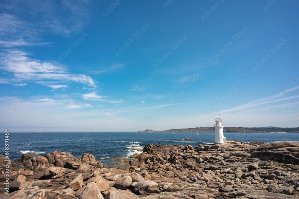 general shot of a seascape with a rocky shore on the coast and a white lighthouse on the right side of the image.