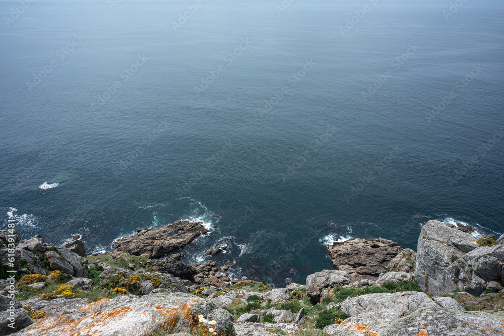 horizontal image from the top of a cliff edge, looking at the rocks overlooking the vastness of the desolate and calm sea.
