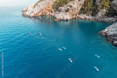 Canvas Print Aerial view of a group or team with paddles swims on a SUP boards on the sea near scenic rocks