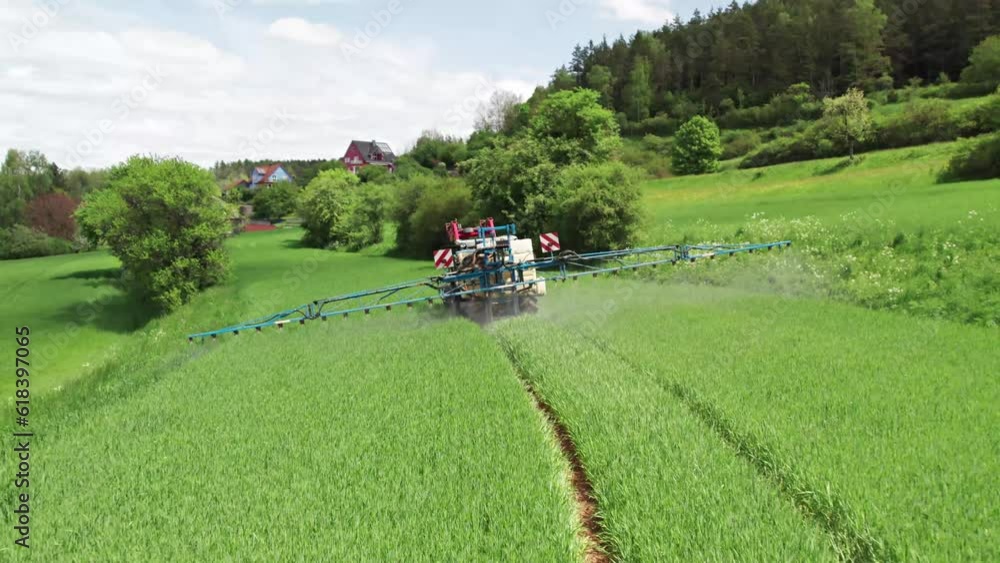 Tractor driven through a lush green field spraying chemicals as it goes Tractor driven through a lush green field spraying chemicals as it goes