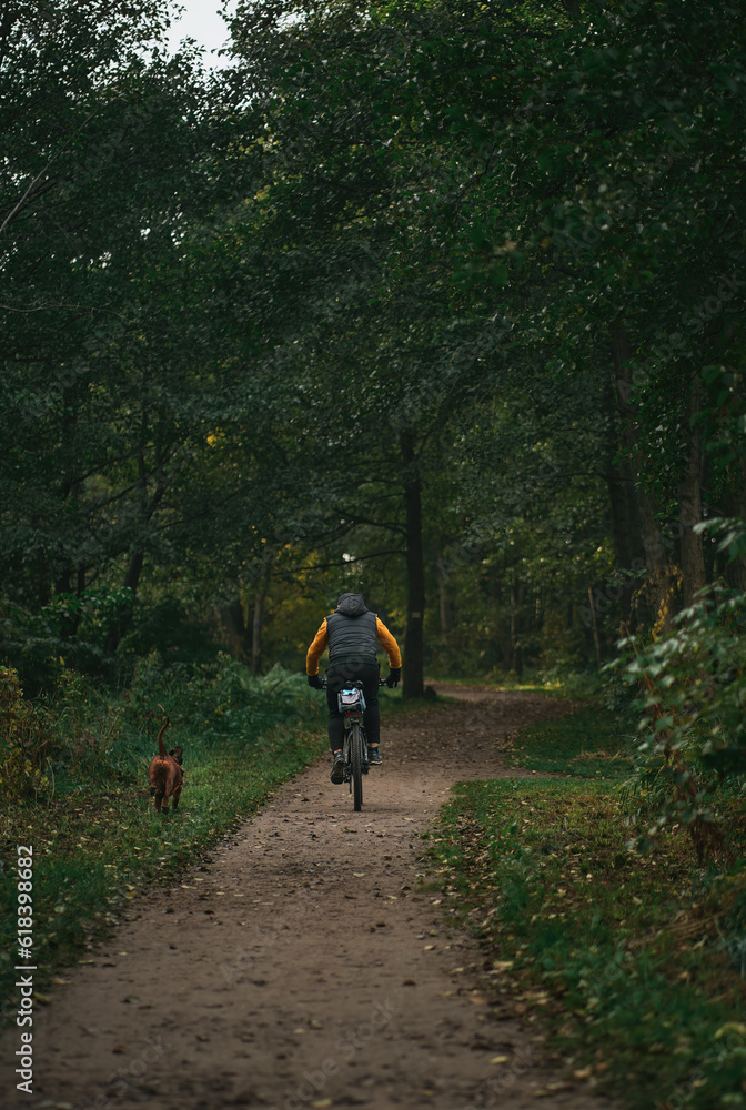 Obraz premium Man rides a bike in the park with his dog