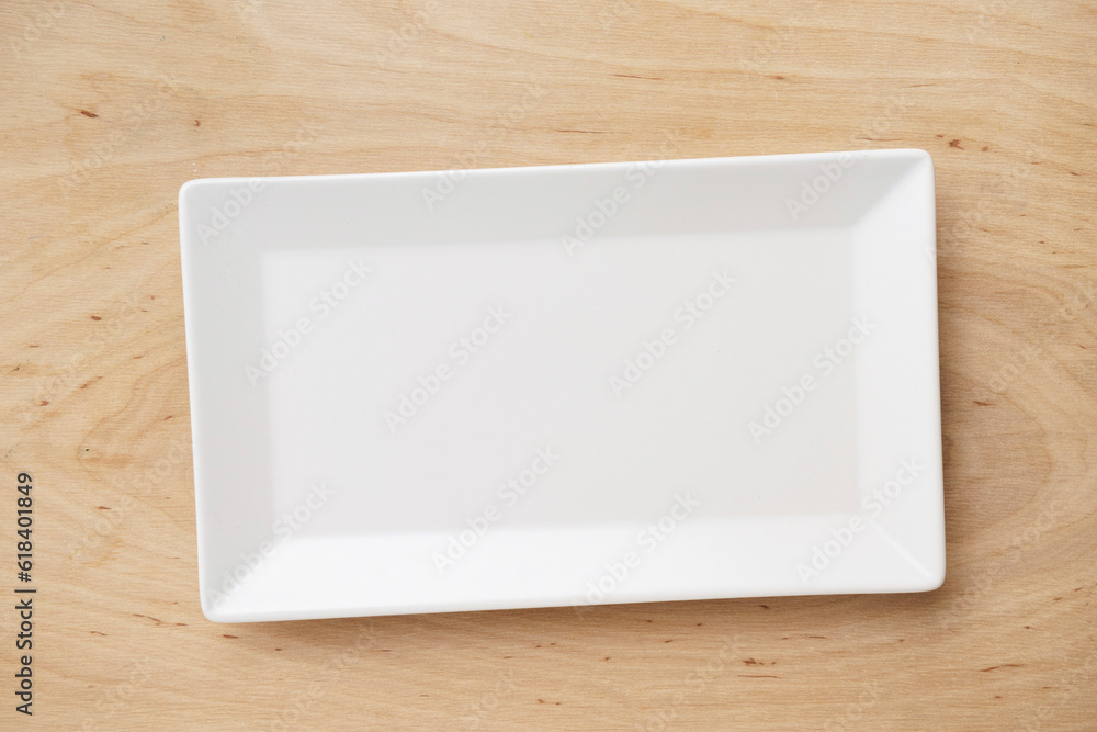 Fotografie White rectangular ceramic plate on a wooden table, top view