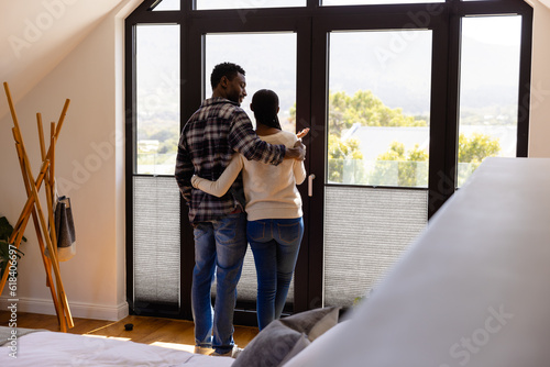 African american couple embracing looking out window in bedroom