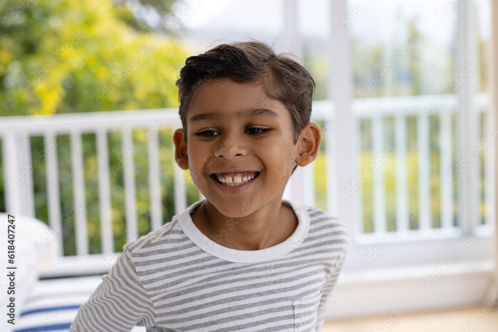 Happy biracial boy smiling in bedroom in front of window with view of garden Happy biracial boy smiling in bedroom in front of window with view of garden