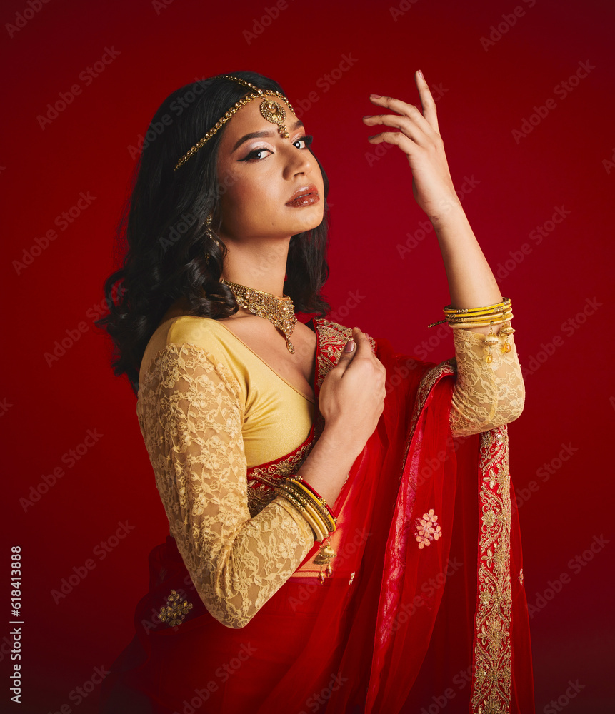 © Tamline L/peopleimages.com - Portrait, confident and Indian woman with fashion, traditional dress and beauty against a red studio background. Face, female person or model with cultural clothes, jewellery and proud with aesthetic