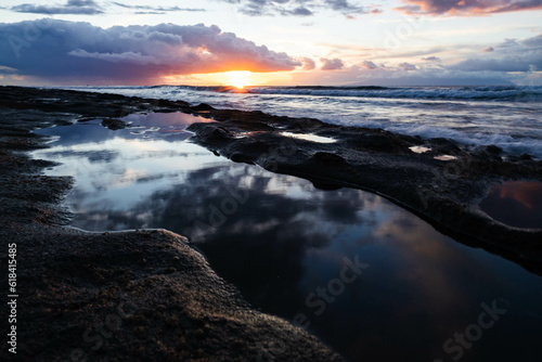 Golden hour on beach. Close up shot of reflection in water. Dramatic sea sunrise. Burning sky and shining golden waves. Reflection of sunlight over water surface. © Stalovyerov