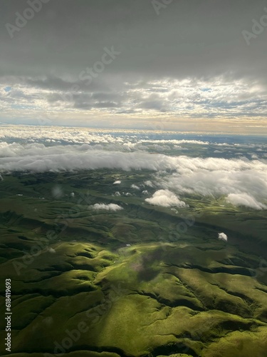 Aerial view of rolling green fields with a backdrop of white puffy clouds in the sky