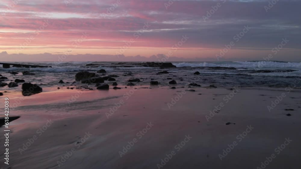 Aerial of the foamy waves of a sea hitting the rocky shore with the pink sunset in the background Aerial of the foamy waves of a sea hitting the rocky shore with the pink sunset in the background