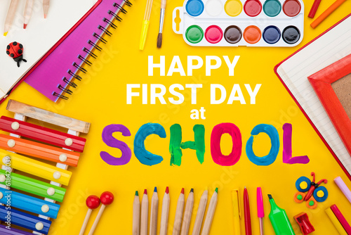 Happy first day of school background. Top view flat lay concept. Childish lettering, colored paper, supplies, stationery for primary school, elementary school or grade school, or preschool educational