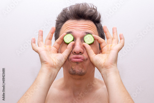 A young man is wrapped in a bath towel after bathing in the bath and doing a cucumber face mask. The concept of caring for male beauty in an ironic form