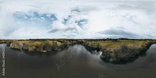 Panoramic shot of a lake surrounded by a forest under a cloudy sky