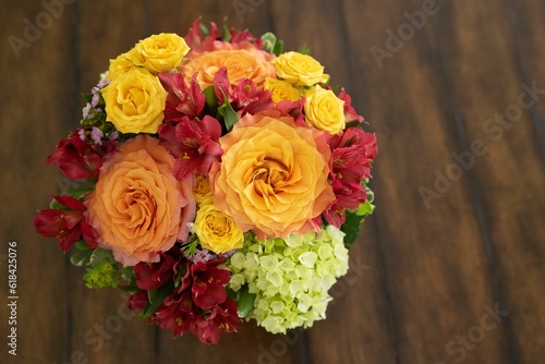 Top view of a stunning floral arrangement of warm-colored roses on a rustic brown wooden table