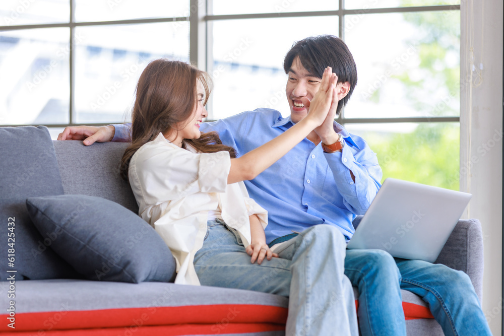 Asian happy cheerful joyful husband and wife lover couple family sitting smiling cuddling together on cozy sofa couch watching streaming movie via laptop notebook computer in living room at home Asian happy cheerful joyful husband and wife lover couple family sitting smiling cuddling together on cozy sofa couch watching streaming movie via laptop notebook computer in living room at home