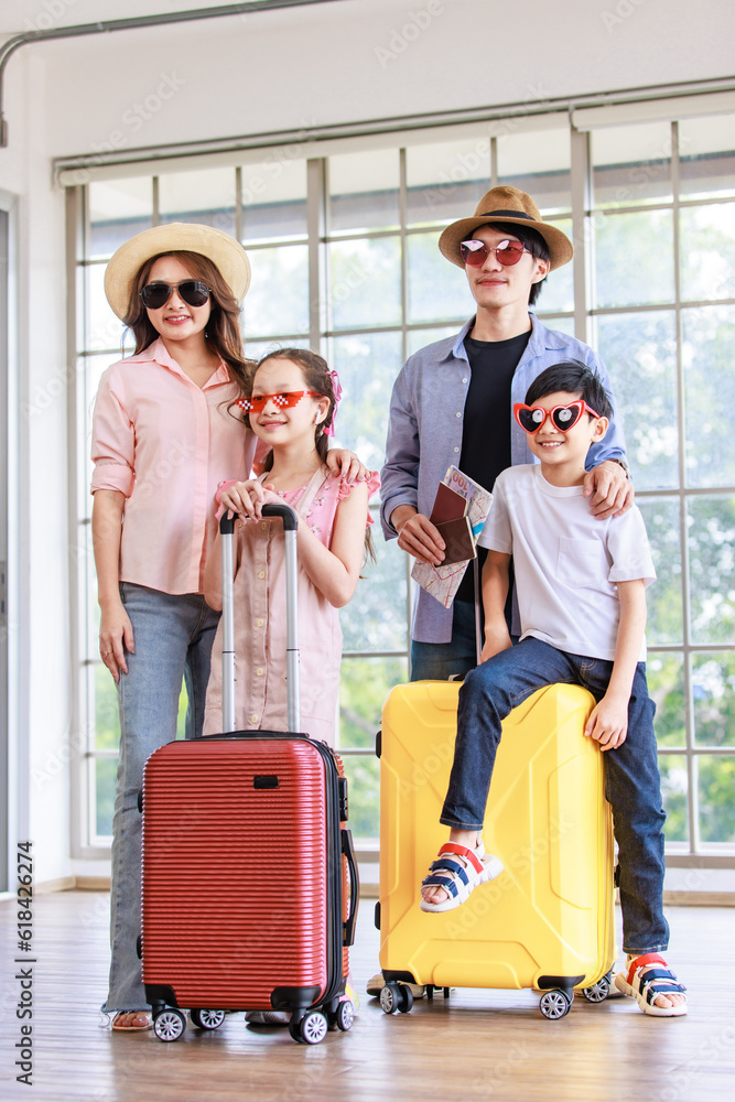 Asian cheerful happy family mom dad son and daughter wearing sunglasses and hat standing posing with two trolley luggages smiling celebrating holiday together ready for traveling vacation road trip