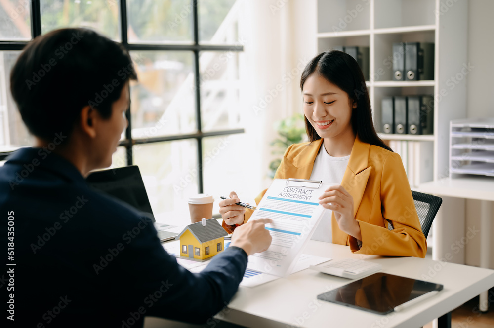 Asian Real estate broker agent presenting and consult to customer to decision making sign insurance form agreement, home model, concerning mortgage loan offer in office Asian Real estate broker agent presenting and consult to customer to decision making sign insurance form agreement, home model, concerning mortgage loan offer in office