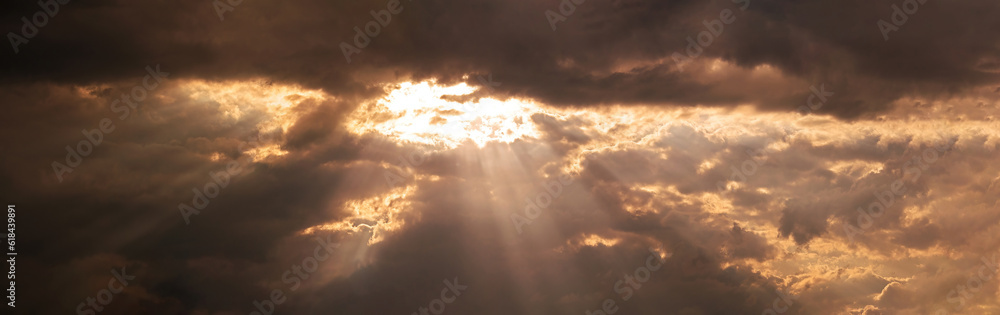 A breathtaking sky panorama showcasing rays of sunlight piercing through gaps in the ominous dark clouds.