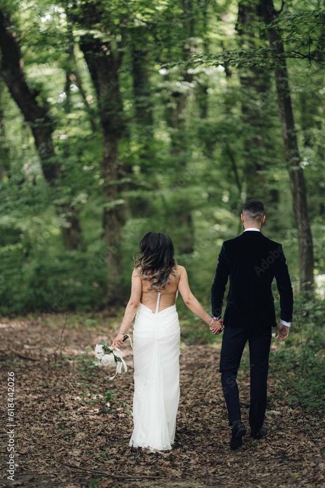 Newly married couple walking hand in hand through a vibrant green forest. Newly married couple walking hand in hand through a vibrant green forest.