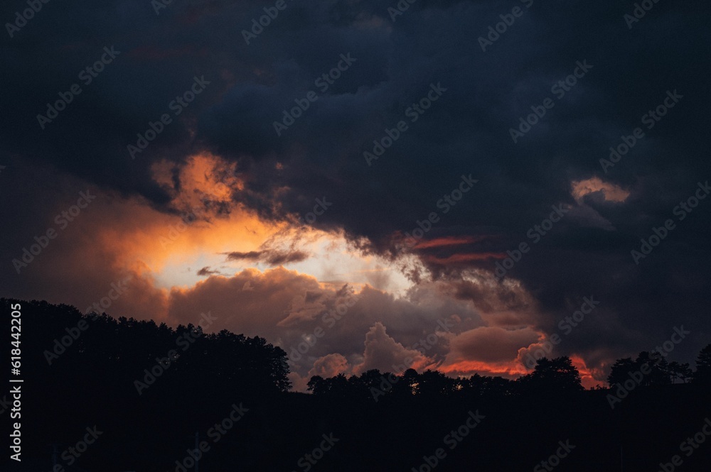 Beautiful scene of a cloudy sunset sky over the silhouette of trees.