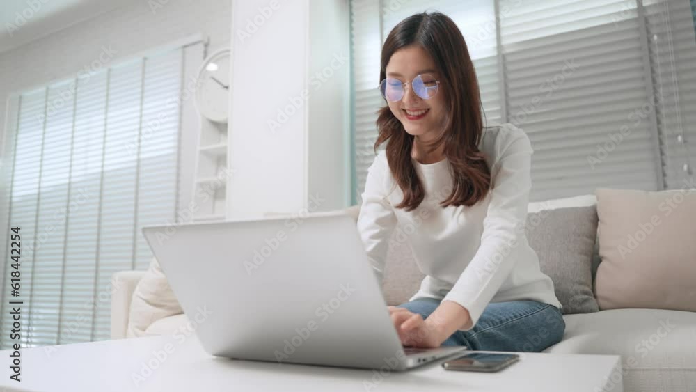 Asian freelance writer using laptop writing an article and sitting on couch at home, Business woman working on computer in living room Asian freelance writer using laptop writing an article and sitting on couch at home, Business woman working on computer in living room