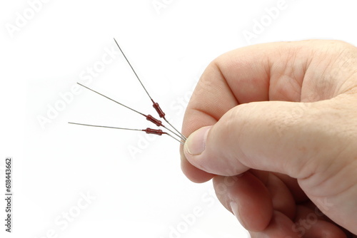 The hand holds three pieces of resistors. Standard electronic components. White background.