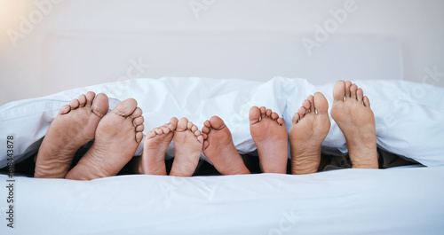 Family, feet in bed and in bedroom of their home with a lens flare sleeping together. Resting or barefoot, morning and parents with toes and children relaxing on holiday weekend break in their house photo