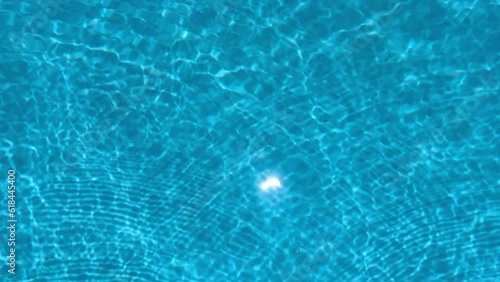 Meditational summer vibe of clear water in the blue swimming pool. Shimmering reflections of the sun create a cinematic view. Ripples on the surface. Spa resort or hotel lounge. photo