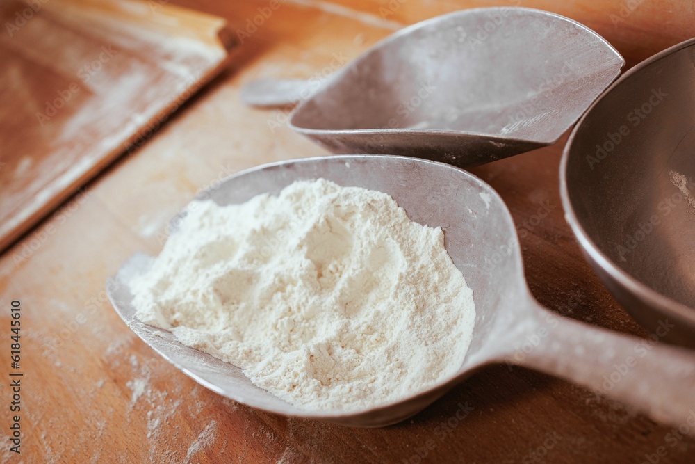 Closeup of a spoons filled with white flour, resting on a rustic wooden Closeup of a spoons filled with white flour, resting on a rustic wooden