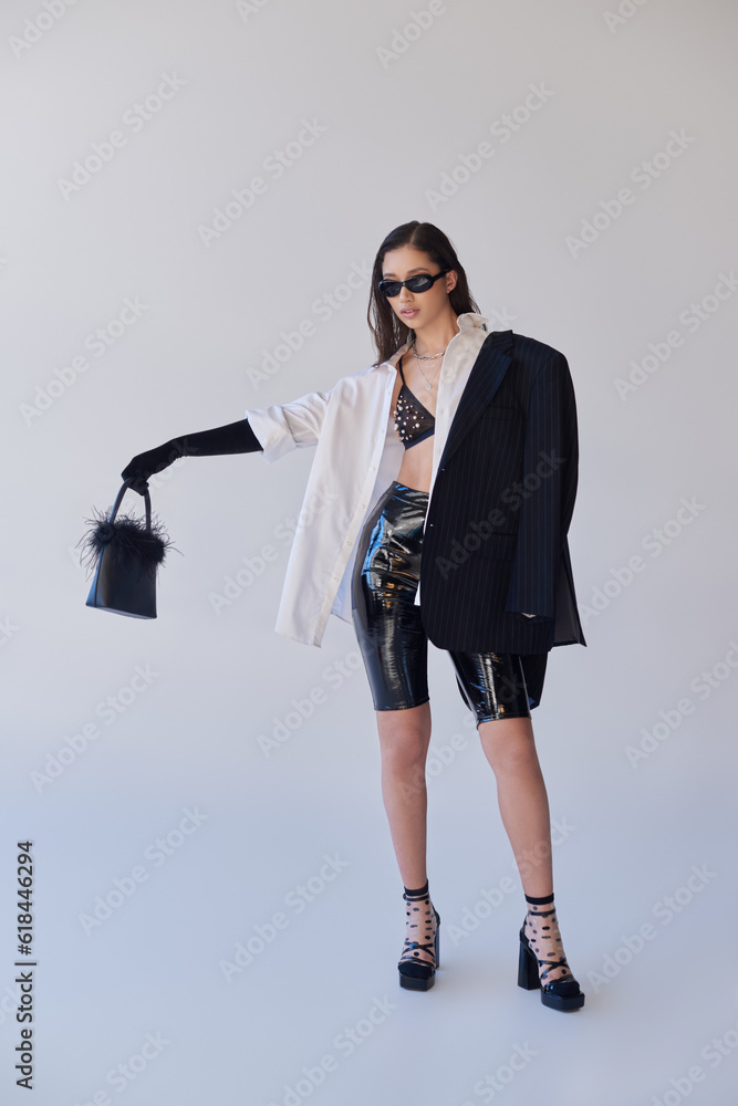 edgy style, studio photography, young asian woman in stylish look and sunglasses posing with feathered handbag on grey background, blazer and latex shorts, youthful fashion, full length edgy style, studio photography, young asian woman in stylish look and sunglasses posing with feathered handbag on grey background, blazer and latex shorts, youthful fashion, full length