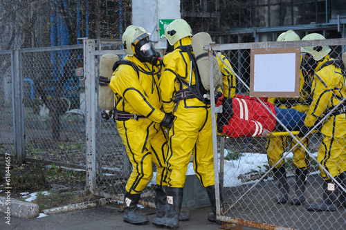 Rescuers in protective rubber suits and masks carrying the sufferer on stratcher from contaminated plant territory. Rescue team training