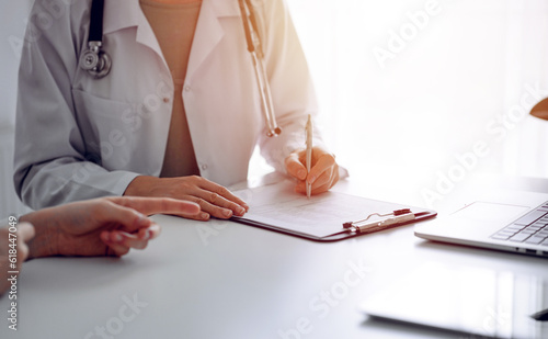 Doctor and patient sitting at the desk in clinic office. The focus is on female physician s hands filling up the medication history record form  close up. Perfect medical service and medicine concept