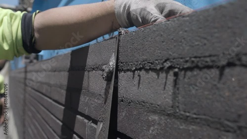 Slow-motion view of a construction worker scraping off excess cement from a brick wall photo