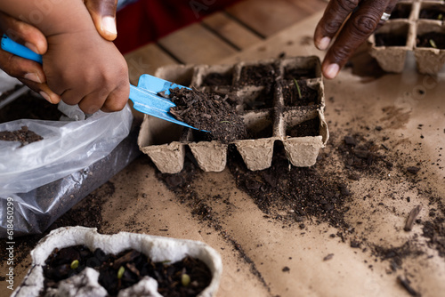 Close up of hands of african american grandfather and grandson planting flowers on terrace