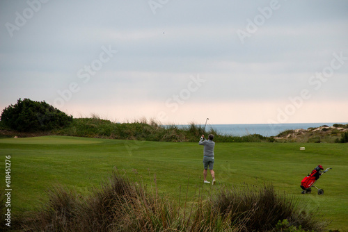 Man playing golf on a green field with the sea in the background
