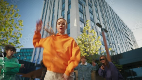 Low Angle Shot: Young And Stylish Female Hip Hop Dancer Freestyling On City Street In Circle Of Fashionable Friends. Group Of Young People Supporting Newstyle Performer, Filming Her On Smartphone. photo