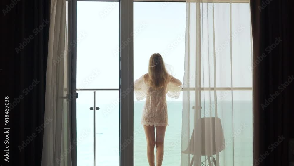 Girl Goes Out to the Balcony and Looks at the Ocean Admiring the Beautiful View on a Summer Vacation in a Comfortable Modern Apartment. Tourism, Travel, Relax. Girl Goes Out to the Balcony and Looks at the Ocean Admiring the Beautiful View on a Summer Vacation in a Comfortable Modern Apartment. Tourism, Travel, Relax.