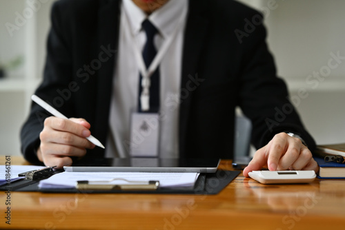 Professional businessman analyzing sales statistics document, using laptop at wooden office desk