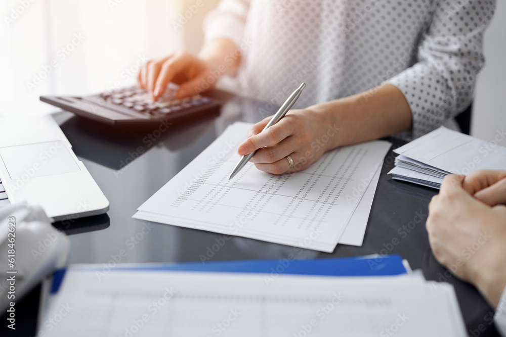 Woman accountant using a calculator and laptop computer while counting taxes for a client. Business audit and finance concepts Woman accountant using a calculator and laptop computer while counting taxes for a client. Business audit and finance concepts