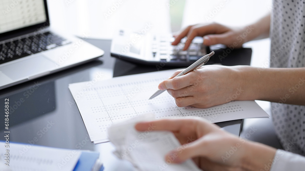 Woman accountant using a calculator and laptop computer while counting taxes with a client or colleague. Business audit team Woman accountant using a calculator and laptop computer while counting taxes with a client or colleague. Business audit team