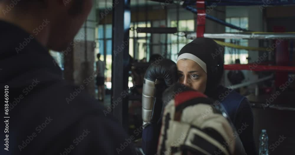 Portrait of Young Determined Arab Woman with Hijab Practicing Boxing in Gym with her Coach. Strong Muslim Female Boxer Working Out and Exercising, Throwing Punchesand Preparing for Competition Portrait of Young Determined Arab Woman with Hijab Practicing Boxing in Gym with her Coach. Strong Muslim Female Boxer Working Out and Exercising, Throwing Punchesand Preparing for Competition