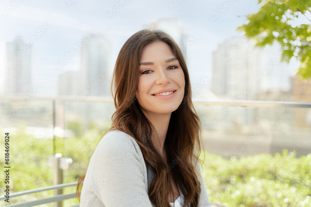 Portrait of attractive smiling woman with beautiful hair looking at camera standing on the street. Happy successful fashion model posing for pictures outdoors