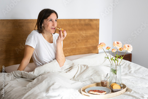 very happy girl sitting in bed having a coffee, toast and cookies for breakfast, with a bouquet of flowers on the tray	
