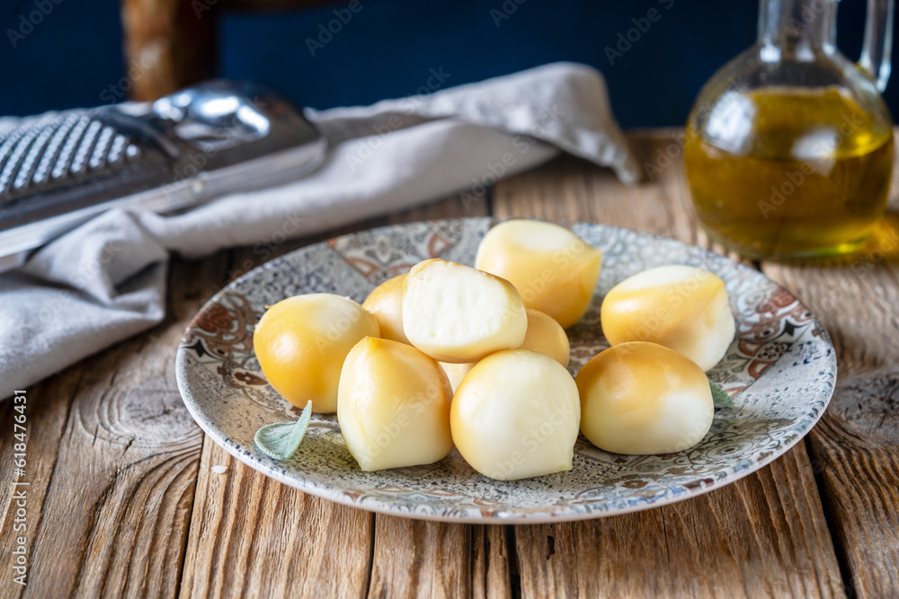 Smoked mozzarella balls in a grey plate with sage leaves, napkin, olive oil, grater over wooden table, chair backside Smoked mozzarella balls in a grey plate with sage leaves, napkin, olive oil, grater over wooden table, chair backside