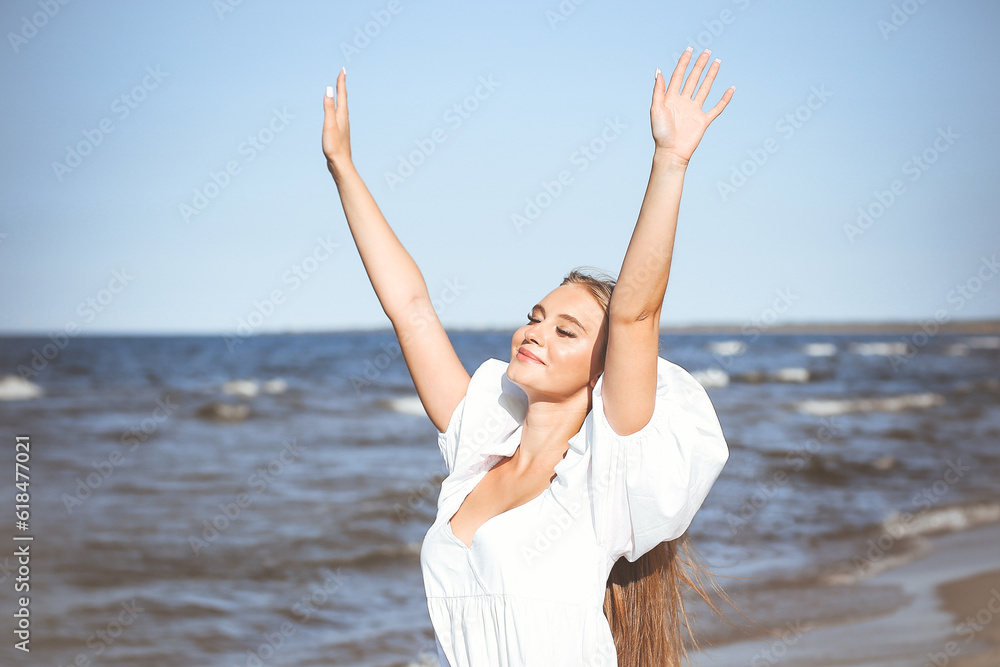 Happy smiling beautiful woman on the ocean beach standing in a white summer dress, raising hands Happy smiling beautiful woman on the ocean beach standing in a white summer dress, raising hands