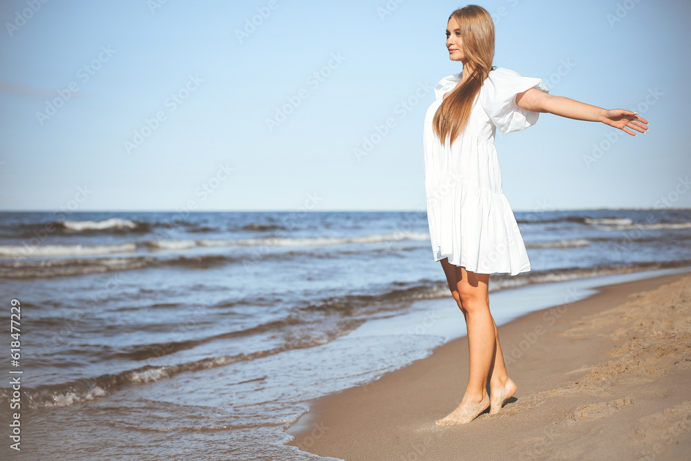 Happy smiling beautiful woman is walking on the ocean beach with open arms Happy smiling beautiful woman is walking on the ocean beach with open arms